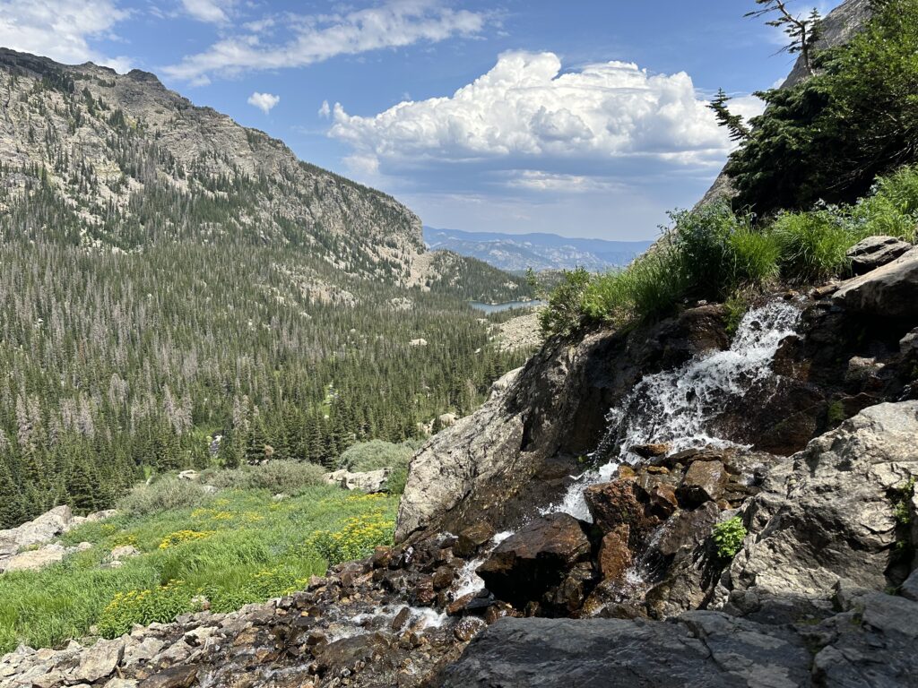 Timberline Falls in the foreground to the right, with mountain scenery and a lake in the background at RMNP