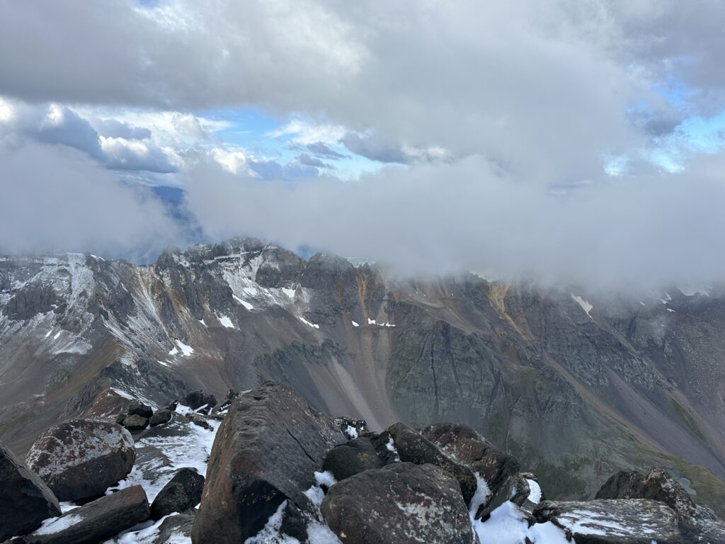 Photo from the top of Mount Sneffels with peaks and clouds in the background